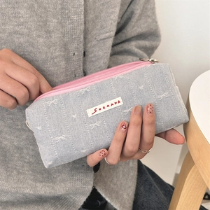 Close-up of denim fabric pencil case with white bow embroidery and pink zipper detail