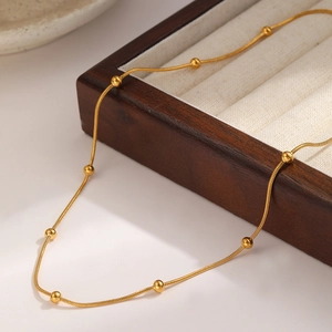 Detail of a minimalist gold beaded chain necklace resting on a premium velvet jewelry box