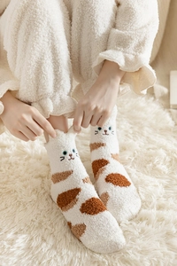 Close-up of cat patterned coral fleece socks on a soft white plush rug for winter warmth