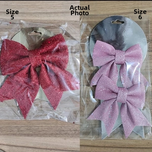 Dettaglio di fiocchi natalizi glitterati rossi e rosa nelle taglie n. 5 e n. 6