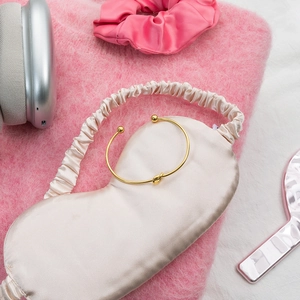 Detail of 18K gold knot cuff bracelet on soft pink fabric with lifestyle accessories