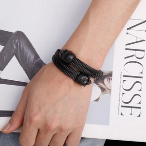 Detail of black dual-cable wire bracelet with skull charms on a fashion magazine