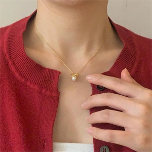 Delicate 925 sterling silver bow and pearl necklace shown on neck with a red cardigan