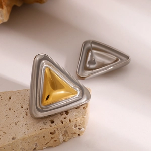Macro detail of two-tone gold and silver triangular earrings on a natural stone surface