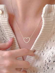 Detail of a gold heart necklace with white zircons worn on a cream knit sweater