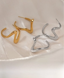 Detail view of twisted gold and silver wavy earrings on elegant white silk background