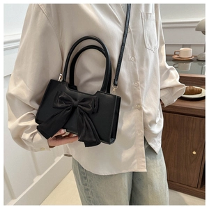 Detail of a black synthetic leather handbag featuring a large bow and a long strap