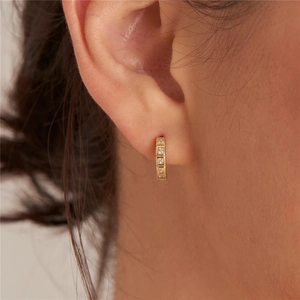 Close-up of gold huggie hoop earring featuring five square-cut cubic zirconia stones