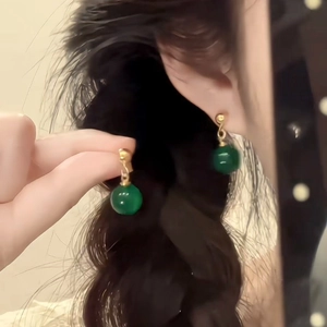 Close-up of vintage gold earrings with emerald green translucent beads on a model