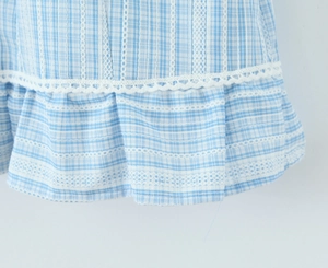 Detailed close-up of blue plaid fabric with white lace trim on the hem of the dress