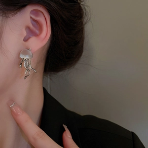 Dettaglio ravvicinato di un orecchino a medusa in argento e resina bianca indossato sull'orecchio