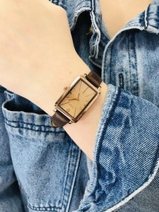 Detail of square rose gold watch with brown leather strap worn on a woman's wrist