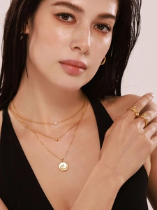 Detail of layered gold necklaces with white sea shell pendant and pearl choker on a model