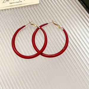 Deep red C-shaped hoop earrings with gold metal posts on a modern textured background