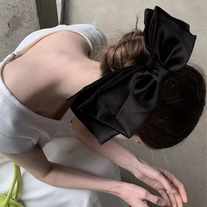 Detail view of a large black satin bow hair clip worn as a stylish ponytail accessory