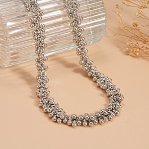 Detailed view of silver bead cluster necklace draped on a textured glass cup