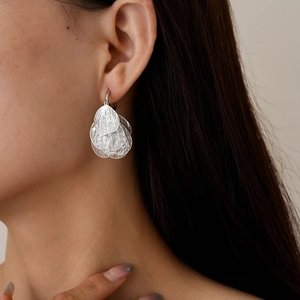 Close-up of silver hollowed leaf-petal earrings worn by a model showing metal texture