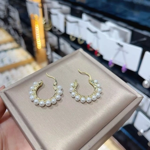 Macro view of gold C-shaped hoop earrings featuring multiple polished white pearls