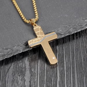 Close-up of gold cross pendant with silver wave details and crystal on a stone surface
