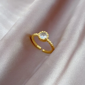 Detailed close-up of a golden open ring with a round zircon stone on silk fabric