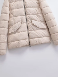 Detail of light beige quilted padded jacket showing the front zipper and side pockets