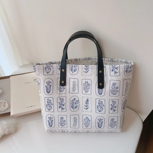 Minimalist white canvas tote bag with blue botanical prints and black leather handles