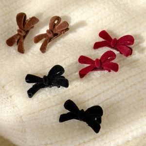 Mini velvet bow hair clips in red, brown, and black colors on a soft knit background