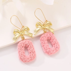Detailed view of golden bow hook and pink resin rose flower square pendant earrings