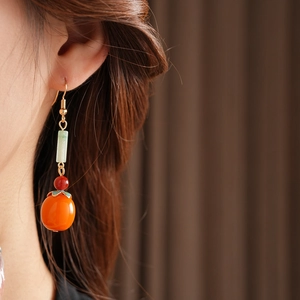 Detail of orange persimmon-shaped agate earrings worn by a model in soft light