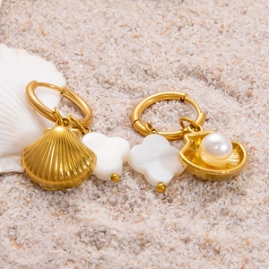 Détails de boucles d'oreilles coquillage doré avec trèfle blanc et perles sur sable