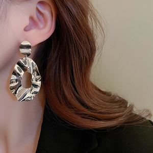 Close-up of silver-toned crumpled geometric hoop earrings worn by a model in profile view