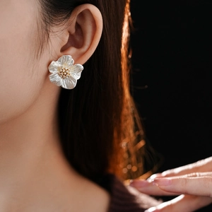 Macro shot of gold-plated flower earrings with white pearl petals worn by a model