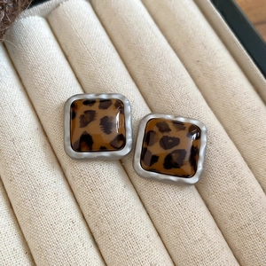Macro shot of square leopard print earrings with matte silver frames in a jewelry box