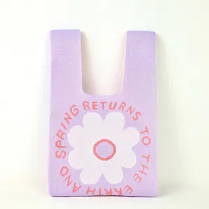 Close-up of a purple knitted tote bag with a white flower pattern and orange text