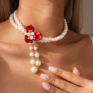 Detail of a double-layer pearl necklace featuring a red flower pendant with pearl tassels