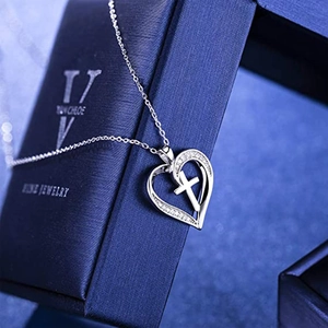 Elegant silver heart and cross pendant necklace with zircon stones on a jewelry box