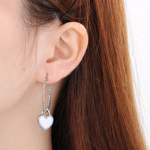 Gros plan d'une créole torsadée argentée avec pendentif cœur blanc sur un mannequin