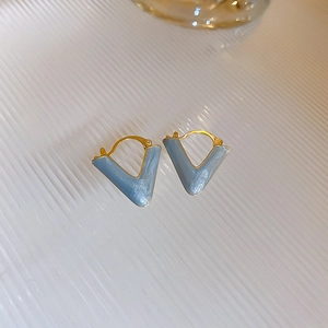 Detailed macro shot of V-shaped gold earrings with light blue enamel on white stripes