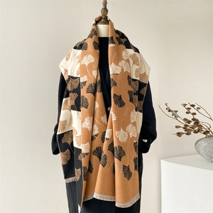 Detail of ginkgo leaf pattern on thick warm scarf draped over a black coat and mannequin