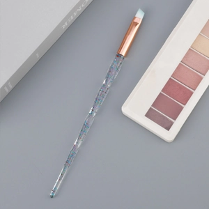 Detail of angled brow brush with glitter handle and rose gold ferrule on a desk