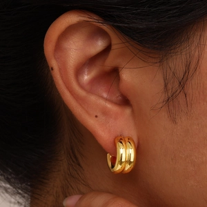 Detailed view of chunky double-layered gold hoop earrings worn on a model earlobe