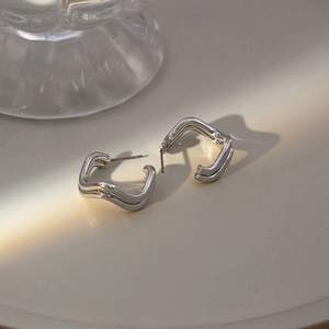 Detailed close-up of geometric silver wave earrings on a minimalist cream background