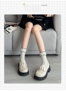 Close-up of cream platform loafers with ruffled socks on a grey wooden floor
