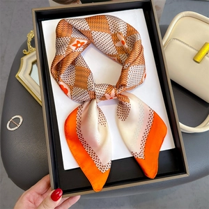 Detailed view of an orange and brown floral silk scarf presented in a luxury gift box