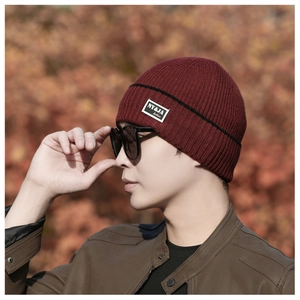 Close-up of a warm dark red knit beanie with black stripes and a woven logo patch