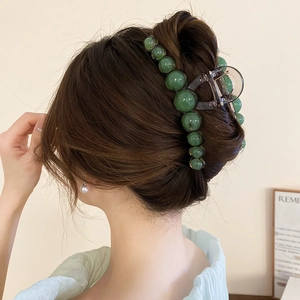 Detail of a large emerald green beaded hair claw clip securing a stylish low bun hairstyle