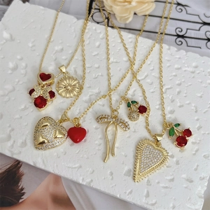 Assorted 18K gold plated necklaces with cherry and heart pendants on stone surface