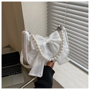 Close-up of white pleated handbag featuring a large silk bow and pearl handle detail