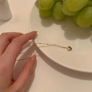 Hand holding a gold 3D heart pendant necklace over a minimalist white ceramic plate