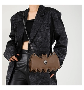 Detail of bat-shaped crossbody bag featuring silver skull emblem and metal chain strap